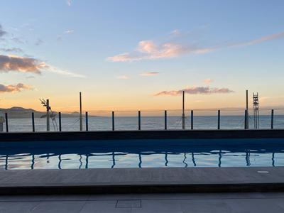 Vue en soirée d'une piscine avec la mer et les montagnes en arrière-plan.