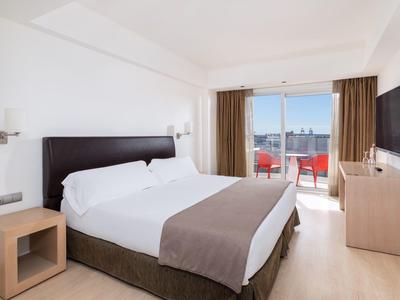 Chambre d'hôtel moderne avec lit double, balcon et vue sur la ville.