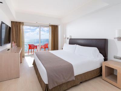 Chambre d'hôtel moderne avec grand lit et balcon offrant une vue sur la mer.