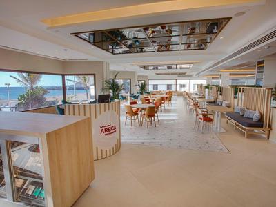 Restaurant lumineux et moderne avec grandes fenêtres et mobilier en bois avec vue sur la mer.