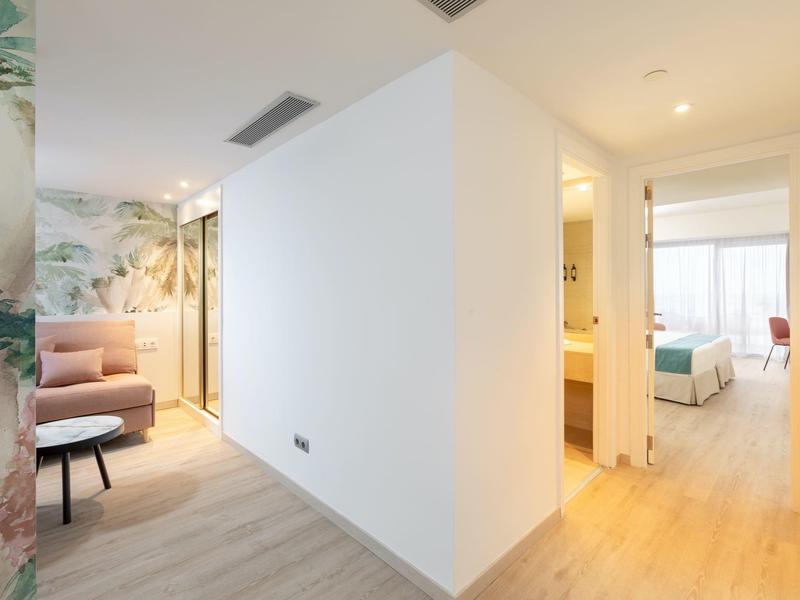 Couloir avec sols en bois clair reliant le salon et la chambre dans un hôtel moderne.