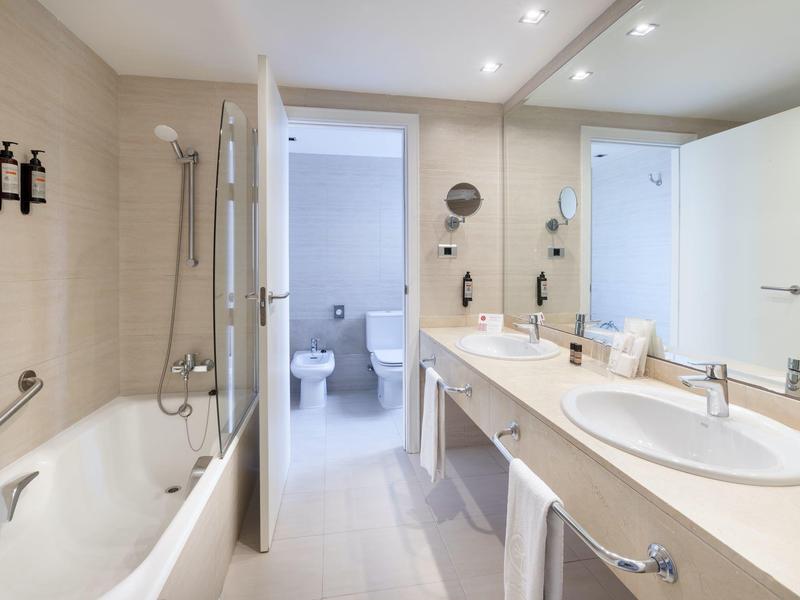 Salle de bain moderne avec baignoire, douche, deux lavabos et vue sur des toilettes séparées.