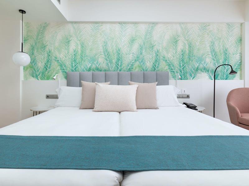 Chambre d'hôtel moderne avec deux lits, fresque végétale et décoration minimaliste.