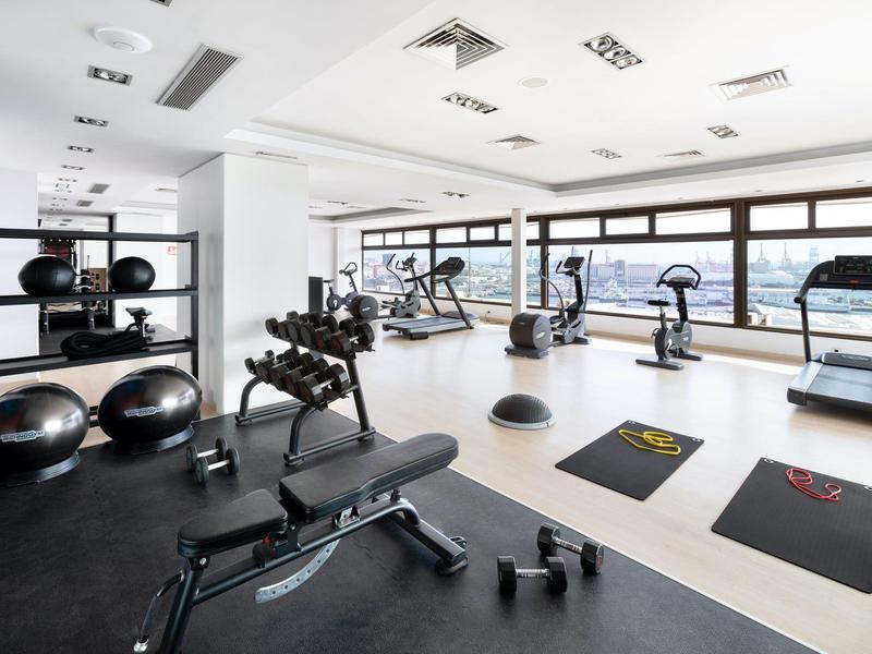 Salle de sport lumineuse avec équipements d'entraînement et grandes fenêtres sur la ville.