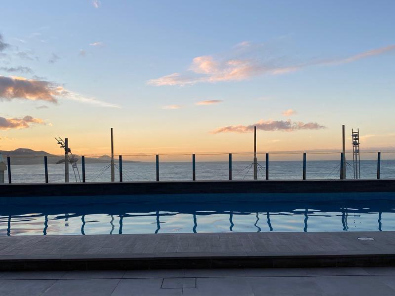 Vue en soirée d'une piscine avec la mer et les montagnes en arrière-plan.