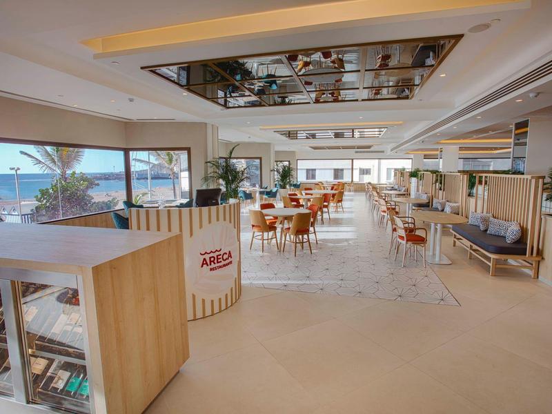 Restaurant lumineux et moderne avec grandes fenêtres et mobilier en bois avec vue sur la mer.