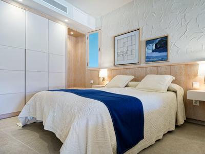Chambre d'hôtel moderne avec grand lit, panneau en bois, murs blancs et couvre-lit bleu.
