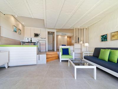 Espace de vie d'hôtel lumineux et moderne avec canapé, table basse et kitchenette aux tons neutres.