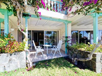 Terrasse avec mobilier de jardin blanc et plantes en fleurs devant une maison de vacances.