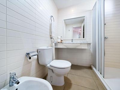 Salle de bain compacte avec toilettes, bidet, lavabo et cabine de douche aux couleurs neutres.