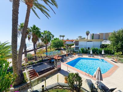 Piscine d'hôtel avec parasols et palmiers sous un ciel bleu clair avec vue sur la mer.
