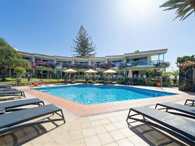 Espace piscine moderne avec transats, parasols et bâtiment hôtel sous un ciel dégagé.