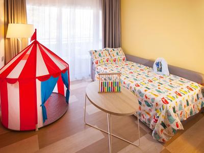 Kinderzimmer mit Einzelbett, bunt gemustertem Bettzeug, rundem Holztisch und rotem Spielzelt.