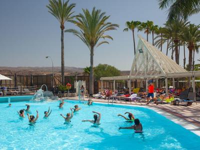 Menschen bei Wassergymnastik im blauen Pool, umgeben von hohen Palmen und Sonnenschirmen.