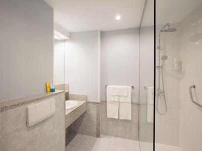 Helles, modernes Badezimmer mit Dusche, Waschbecken, Spiegel und beigen Fliesen an Wänden und Boden.