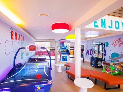 Bunte Spielhalle mit Airhockey-Tisch, Automaten und moderner Beleuchtung, helle Wände mit Schrift.