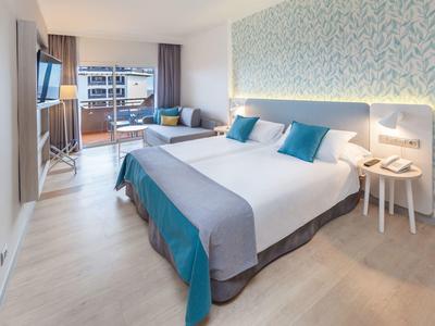 Hell eingerichtetes Schlafzimmer mit großem Bett, blauen Kissen und Balkon mit Ausblick.