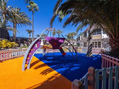 Colorful playground with climbing frame in a hotel setting on a sunny day.