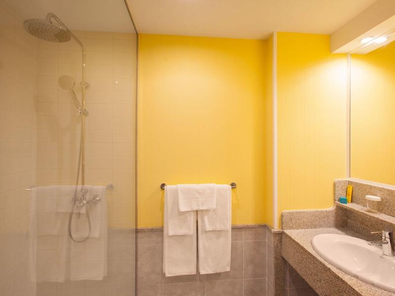 Salle de bain moderne avec murs jaunes, grand miroir, doubles lavabos et espace douche.