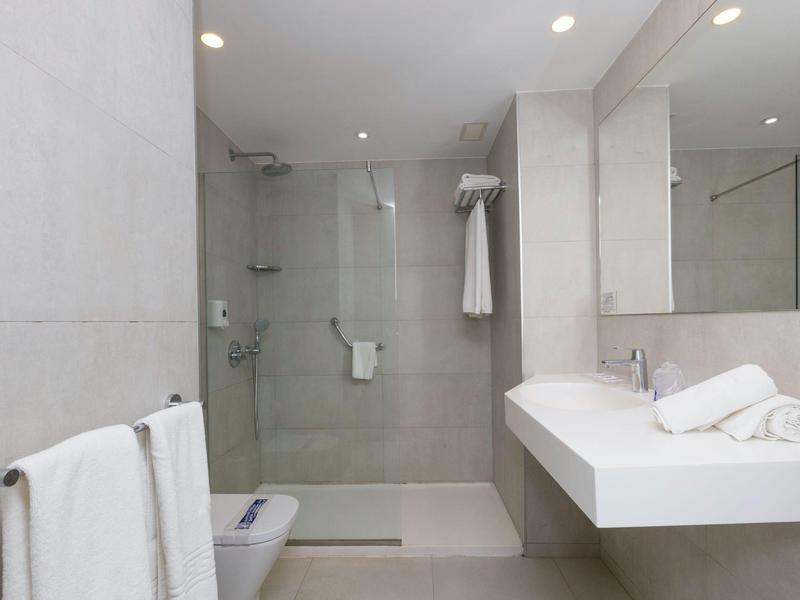 Nowoczesna łazienka hotelowa z prysznicem bez brodzika, białymi ręcznikami i dużym lustrem.