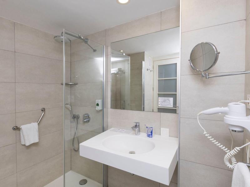 Nowoczesna łazienka z prysznicem, umywalką, dużym lustrem i suszarką naścienną.