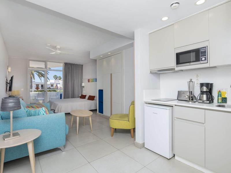 Jasno urządzone mieszkanie z aneksem kuchennym, częścią wypoczynkową i oknem z widokiem na zewnątrz.