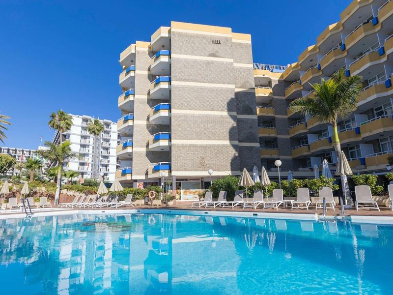 Nowoczesny kompleks hotelowy z basenem, leżakami i palmami pod czystym niebem.