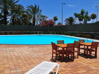 Ein Pool mit klarem Wasser, umgeben von Palmen, Terrassenmöbeln und einer Liege unter einem Sonnenschutz.