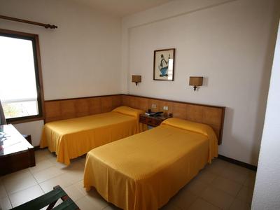 Prosty pokój hotelowy z dwoma łóżkami pojedynczymi i żółtymi narzutami, okno z zasłoną.