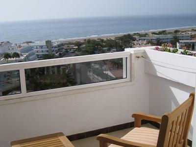 Balkon z drewnianym krzesłem i stołem z widokiem na morze i wybrzeże przy czystym niebie.