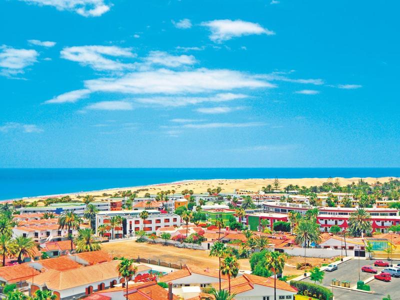 Widok na nadmorskie miasto z piaszczystą plażą, niebieskim morzem i pochmurnym niebem.