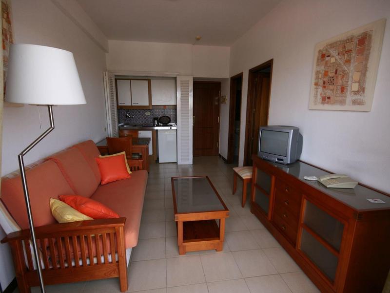 Przytulny salon z sofą, lampą stojącą, małym stolikiem i telewizorem w apartamencie hotelowym.