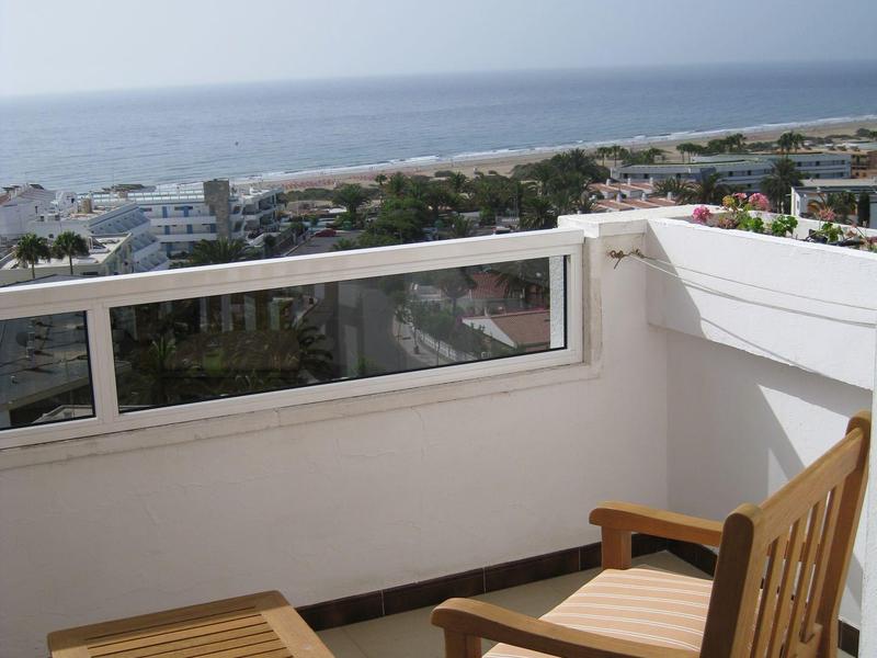 Balkon z drewnianym krzesłem i stołem z widokiem na morze i wybrzeże przy czystym niebie.