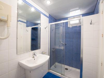 Kleines Badezimmer mit weißem Waschbecken, Glas-Duschkabine und blauen Wandfliesen.