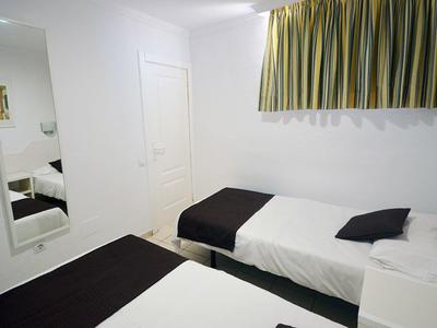 Schlichtes Zimmer mit zwei Einzelbetten, weißen Wänden, grün-gelbem Vorhang und langem Spiegel.