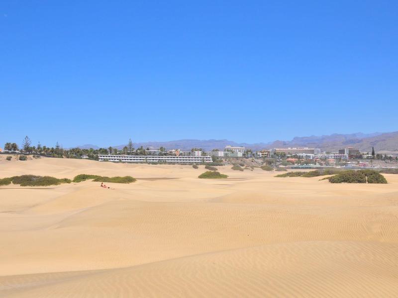 Weite Sanddünen mit einer Stadt und Bergen im Hintergrund unter klarem blauem Himmel