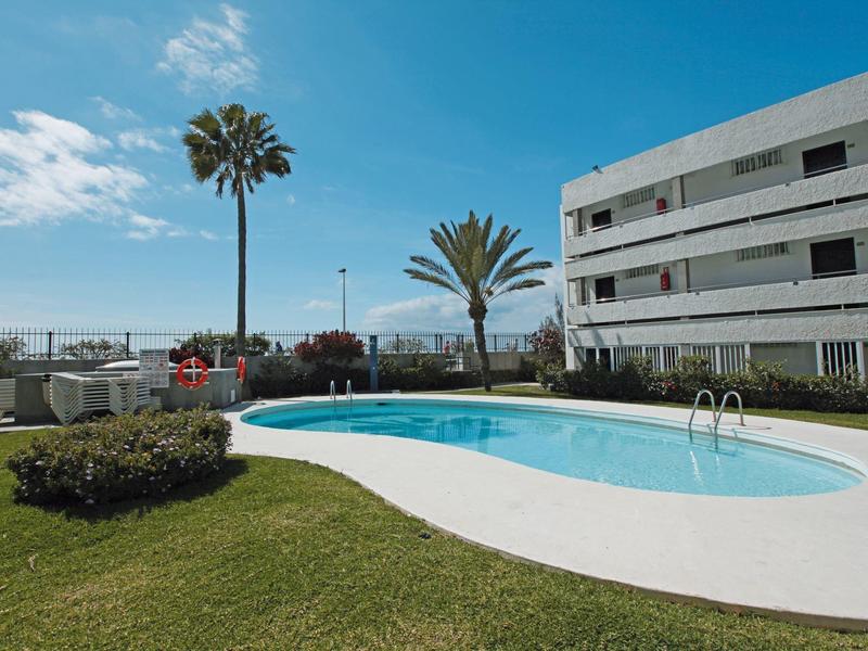 Außenpool und Rasenfläche neben einem weißen Hotelgebäude unter blauem Himmel
