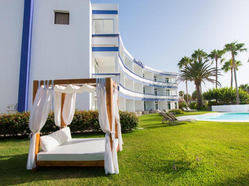 Gemütliche Hängematte mit weißen Vorhängen im Garten eines modernen Hotels mit Pool und Palmen.