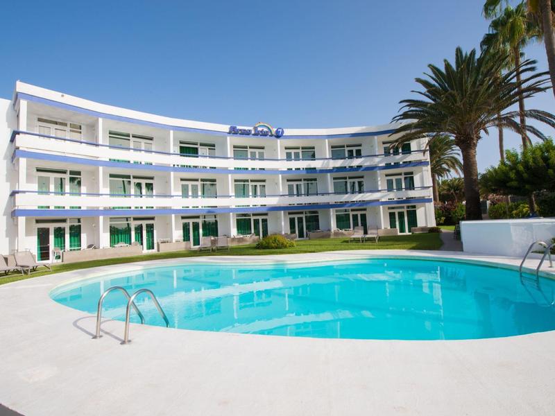 Modernes Hotelgebäude mit rundem Pool und Palmen unter klarem Himmel