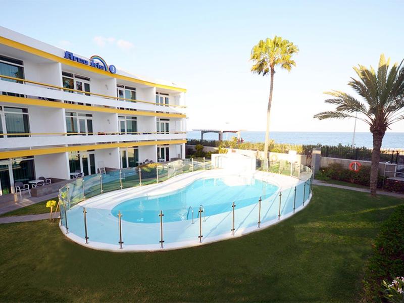 Moderner Schwimmbadbereich mit ovalem Pool, Glaszaun, Palmen und drei Stockwerken Wohngebäude.