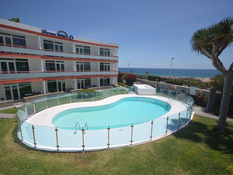 Außenpool mit Glasgeländer neben einem modernen Hotelgebäude, Meer im Hintergrund.