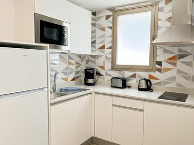 Cuisine d'hôtel blanche compacte avec réfrigérateur, micro-ondes et cafetière sous une fenêtre.
