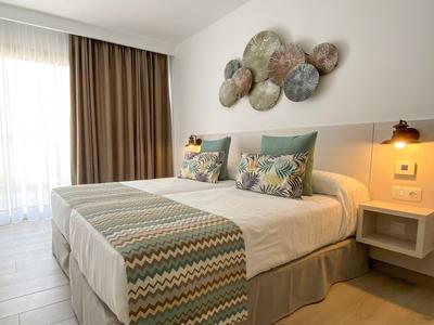 Chambre d'hôtel moderne avec lit double, coussins décoratifs et grande fenêtre avec rideaux.