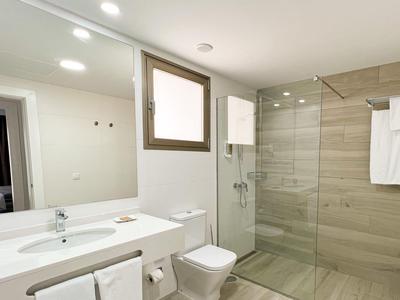 Salle de bain d'hôtel lumineuse et moderne avec douche en verre, toilettes et grand miroir au-dessus du double lavabo.