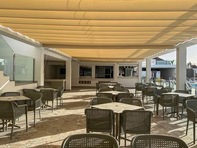 Terrasse extérieure couverte avec plusieurs tables et chaises dans un espace lumineux d’hôtel.