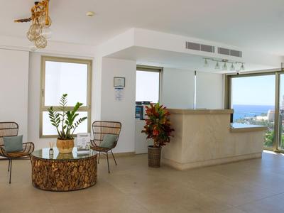 Réception d'hôtel moderne avec comptoir en bois naturel, espace salon et vue sur la mer par de grandes fenêtres.