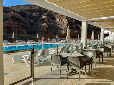 Terrasse couverte avec chaises et tables à côté d'une piscine, entourée de paysage rocheux.