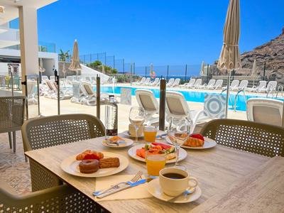Une table dressée avec petit-déjeuner devant une piscine avec vue sur la mer et les falaises.