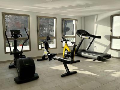 Salle de sport avec équipements modernes et grandes fenêtres laissant entrer la lumière naturelle.