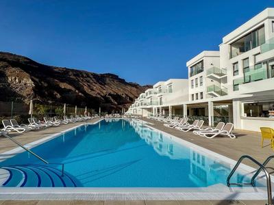 Piscine claire dans un hôtel moderne avec des chaises longues et des montagnes en arrière-plan.